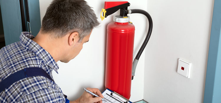 Our fire warden training courses help employers fulfil their legal obligations to protect their employees Photo of a worker carrying out a routine inspection of fire extinguishers in an office